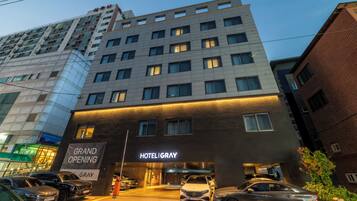 Un hotel con fachada moderna, varios pisos y una entrada destacada con un cartel que anuncia su inauguración.
