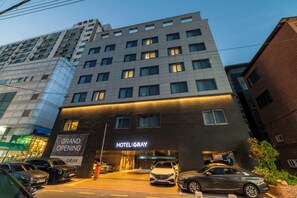 Un hotel con fachada moderna, varios pisos y una entrada destacada con un cartel que anuncia su inauguración.