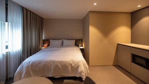 A hotel room with a large bed, a desk, a wardrobe, and a window with curtains. - Gray Hotel (Yongin)