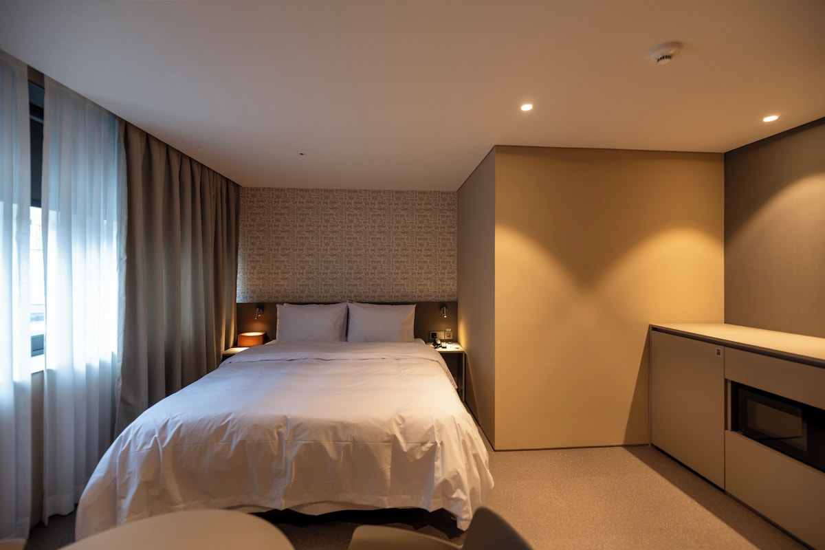 A hotel room with a large bed, a desk, a wardrobe, and a window with curtains.