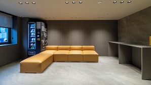 A modern waiting area with a sectional sofa, a vending machine, and a small counter. - Gray Hotel (Yongin)