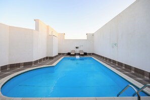 A rectangular indoor swimming pool with a tiled border, two lounge chairs, and a pool depth sign. - Abraj Inn Suites Hotel (Doha)