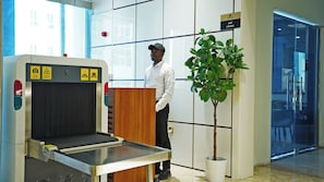 A man standing next to a podium in a room with a glass partition, a potted plant, and a sign indicating a lounge area. - Abraj Inn Suites Hotel (Doha)