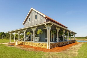 A two-story house with a covered porch, stone foundation, and a view of a lake.