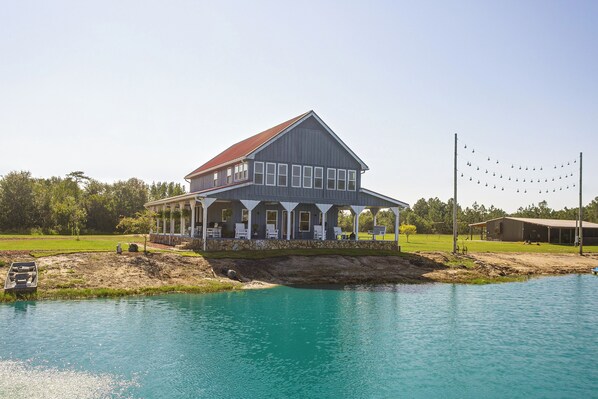 A large two-story house with a porch, a swimming pool, and a dock extending into the water.