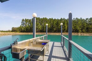 A pier with a metal sink and a blue basin, overlooking a turquoise body of water with a forested shoreline.