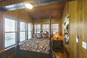 A four-poster bed with a floral bedspread, wooden walls, and a ceiling light fixture.