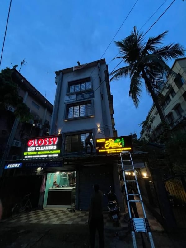 A multi-story building with commercial spaces on the ground floor, including a dry cleaners and a shop with neon signage. - Shree Shyam Guest House (Siliguri)