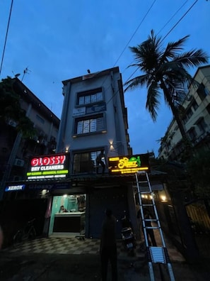 A multi-story building with commercial spaces on the ground floor, including a dry cleaners and a shop with neon signage.
