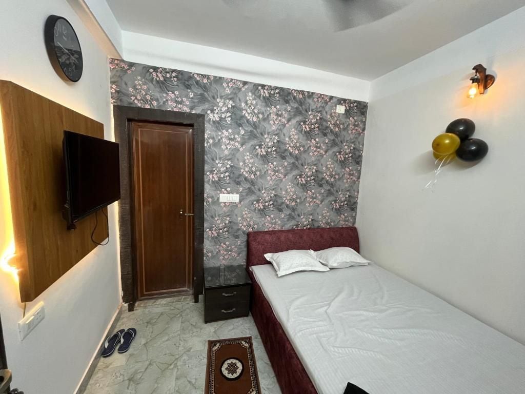 Un dormitorio con una cama, un televisor de pared, una puerta y una pequeña alfombra.