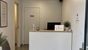 Zona de recepción de hotel con mostrador, una silla, una planta en maceta, un cartel que indica disponibilidad de Wi-Fi y una puerta con la inscripción 'Solo personal'.