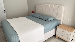 Un dormitorio con una cama, una mesita de noche y un enchufe en la pared.