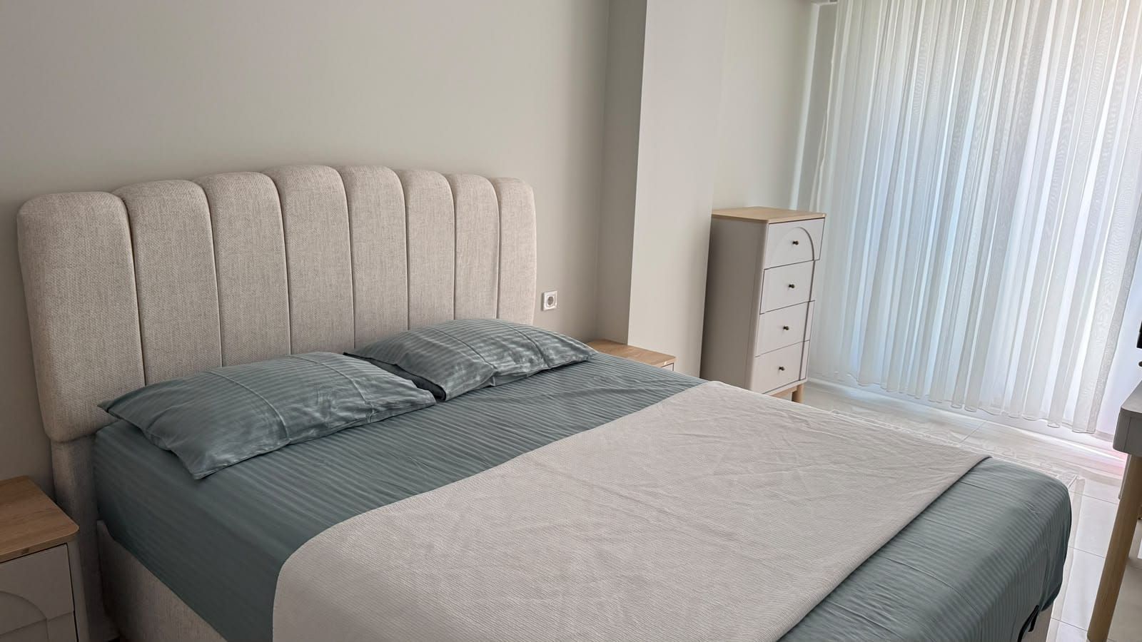 A bedroom with a bed, a nightstand, a dresser, and a window with curtains.
