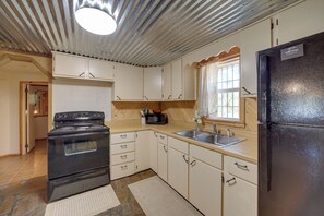 A compact kitchen with a black stove, white cabinets, a black refrigerator, and a window with decorative curtains. - Lake Country Retreat Near Eufaula Adventures (Eufaula)