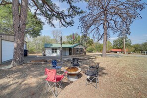 A backyard with a fire pit, two folding chairs, and a small house with a green roof. - Lake Country Retreat Near Eufaula Adventures (Eufaula)