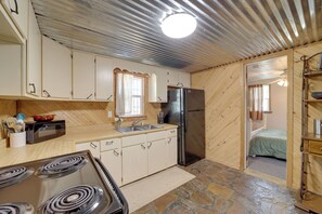 A compact kitchen with a stove, refrigerator, and wooden cabinets. - Lake Country Retreat Near Eufaula Adventures (Eufaula)