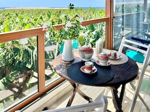 A balcony with a table set for tea, a vase with flowers, and a view of a green field. - Holiday Home in Fuencaliente for 3 (Fuencaliente de la Palma)