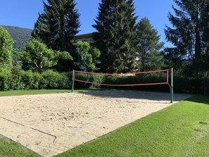 A sandy volleyball court with a net, surrounded by grass and trees. - Directly on Lake Ossiach 1 (Steindorf am Ossiacher See)