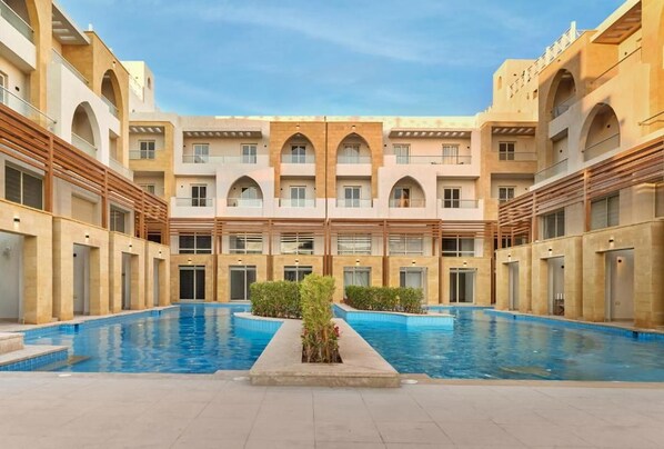 Un patio de hotel con piscina central, varios balcones y un diseño arquitectónico moderno.
