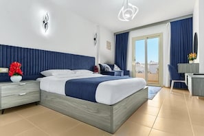Un dormitorio moderno con una cama grande, una mesita de noche con un florero, un escritorio con una silla y vistas a través de un ventanal.