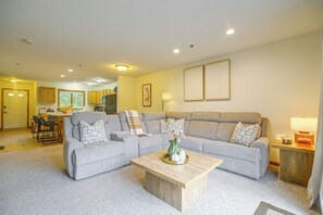 A living room with a grey sectional sofa, a coffee table, and a kitchen in the background. - Mountain-View Cedar Creek Condo w/ Trail Access (Conway)