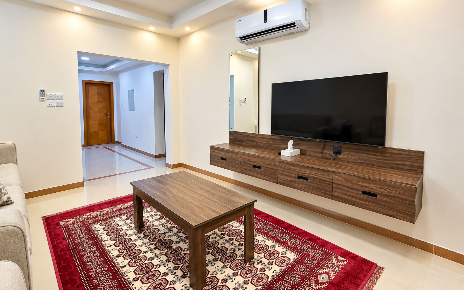 A modern living room with a flat-screen TV, wooden entertainment unit, and a red patterned rug.