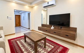 Una sala de estar moderna con un televisor de pantalla plana, un mueble de entretenimiento de madera y una alfombra roja estampada.