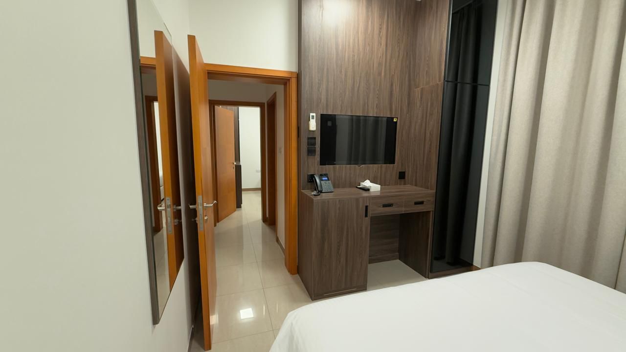 A hotel room with a bed, a desk with a flat-screen TV, a telephone, and a mirror.