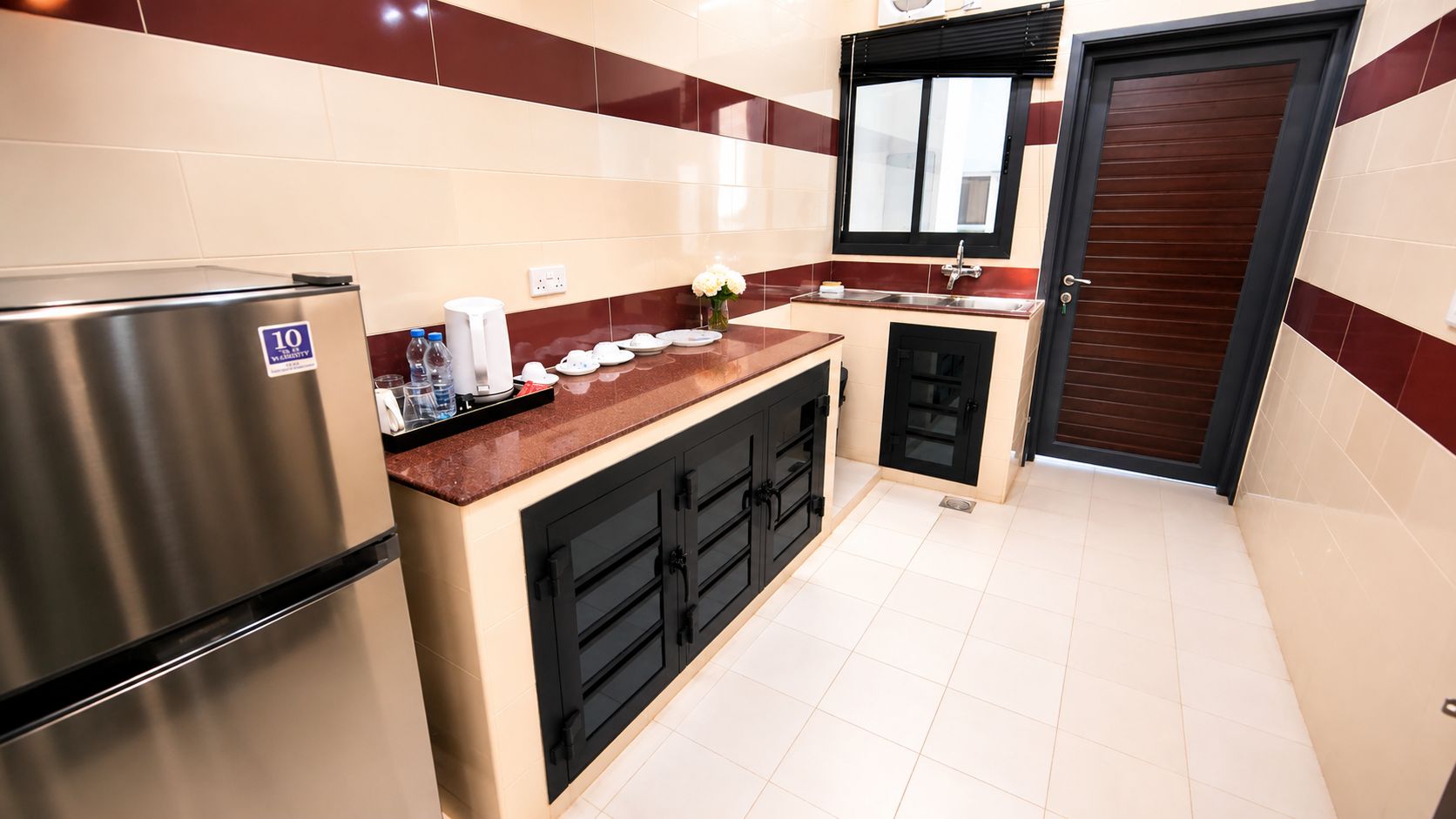 A compact kitchen with a stainless steel refrigerator, a countertop with various items, and a black door.