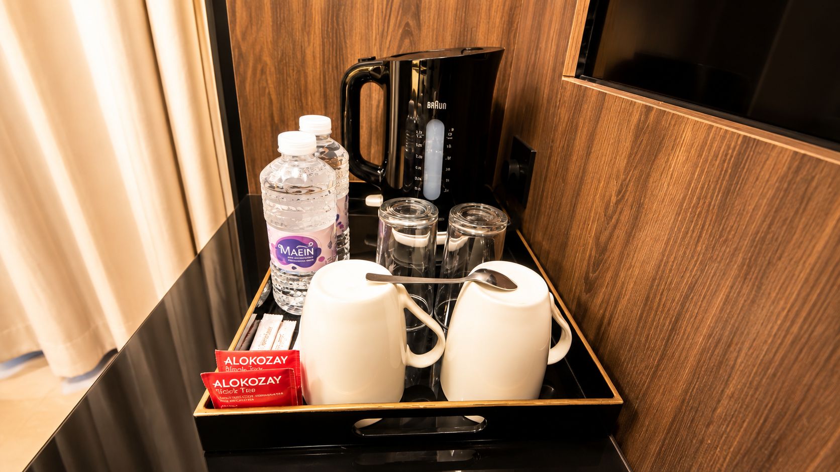 Una bandeja amb una ampolla d'aigua, gots, una cafetera i un joc de te a una habitació d'hotel.
