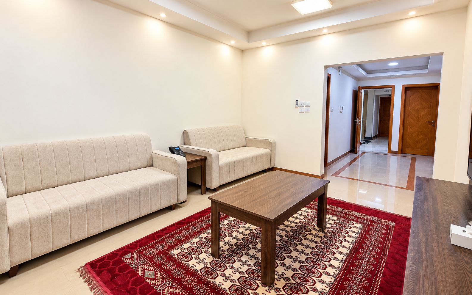A living room with a sofa, armchair, and coffee table, a patterned rug, and a hallway leading to another room.