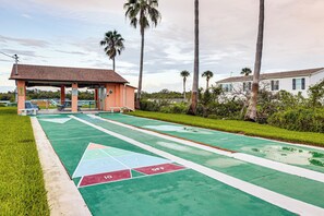 A shuffleboard court with a pavilion, palm trees, and a residential building in the background. - Boat Ramp, Fishing Pier & Game Room Retreat (Edgewater)