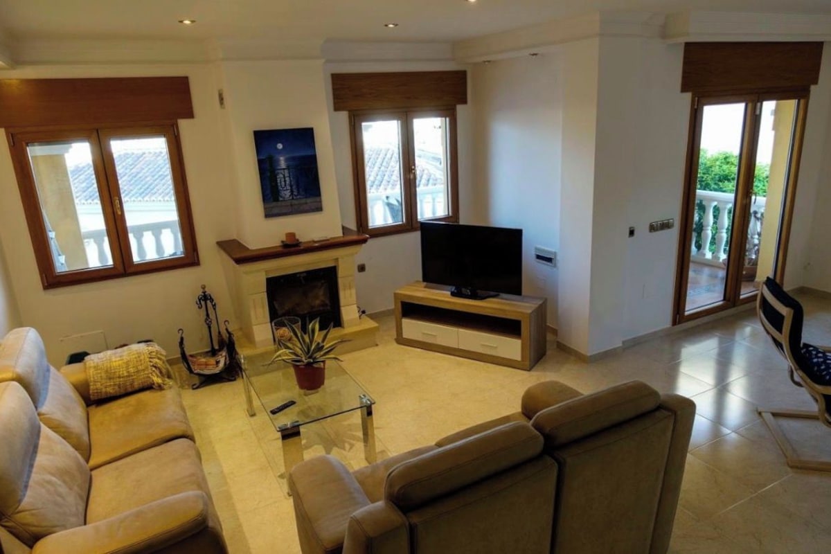 Una sala de estar con sofá, televisión, chimenea y puerta al balcón.