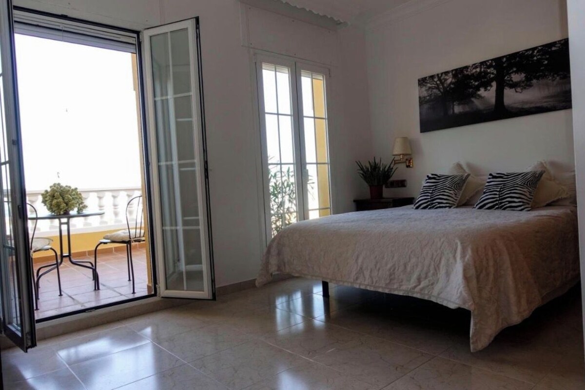 Un dormitorio con una cama, un ventanal corredero a un balcón y un cuadro en la pared.