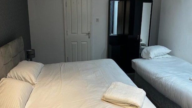 A hotel room with two beds, a white door, and a mirror. - Standard Triple Room - Shared (Manchester)