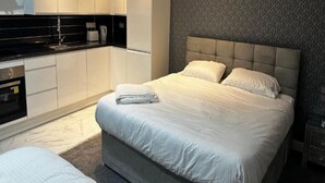 A modern hotel room with a large bed, a separate seating area, a kitchenette, and a patterned wall. - Standard Triple Room - Shared (Manchester)
