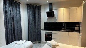 A hotel room with two beds, a kitchenette, and a flat-screen TV. - Standard Triple Room - Shared (Manchester)
