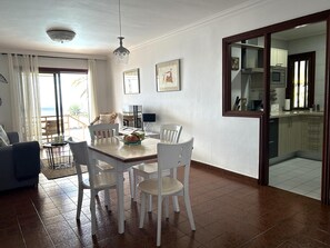 A dining area with a table and chairs, a sofa, a lamp, and a view of the outside. - Apartment in Radazul by the sea (El Rosario)