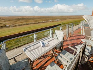A terrace with a table and chairs, overlooking a flat landscape with a fence and a distant horizon. - Holiday Apartment in Juist With Swimming Pool (Juist)