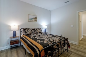 A bedroom with a bed, two bedside lamps, a nightstand, a wall-mounted picture, and a door leading to another room. - Walk to Beach! Windmark Family Home (Port St Joe)