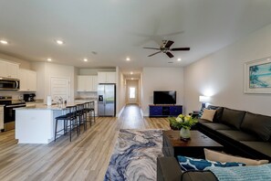 A modern kitchen with a central island, a dining area with a black leather sofa, and a living room with a flat-screen TV. - Walk to Beach! Windmark Family Home (Port St Joe)