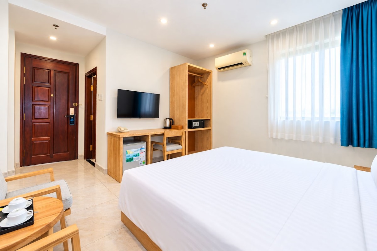 A hotel room with a bed, a desk with a computer, a television, and a minibar.