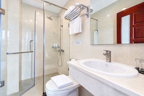 A modern bathroom with a glass shower enclosure, a white toilet, a sink with a mirror above, and a cabinet with a towel rack. - Nam Châu Stellar Hotel (Phu Quoc)