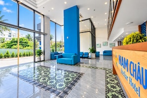 A hotel lobby with a reception desk, blue seating, and large windows. - Nam Châu Stellar Hotel (Phu Quoc)