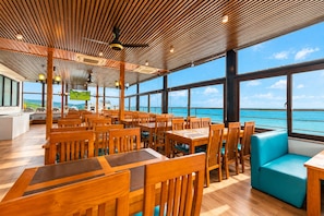 A restaurant with wooden furniture and large windows overlooking the sea. - Nam Châu Stellar Hotel (Phu Quoc)