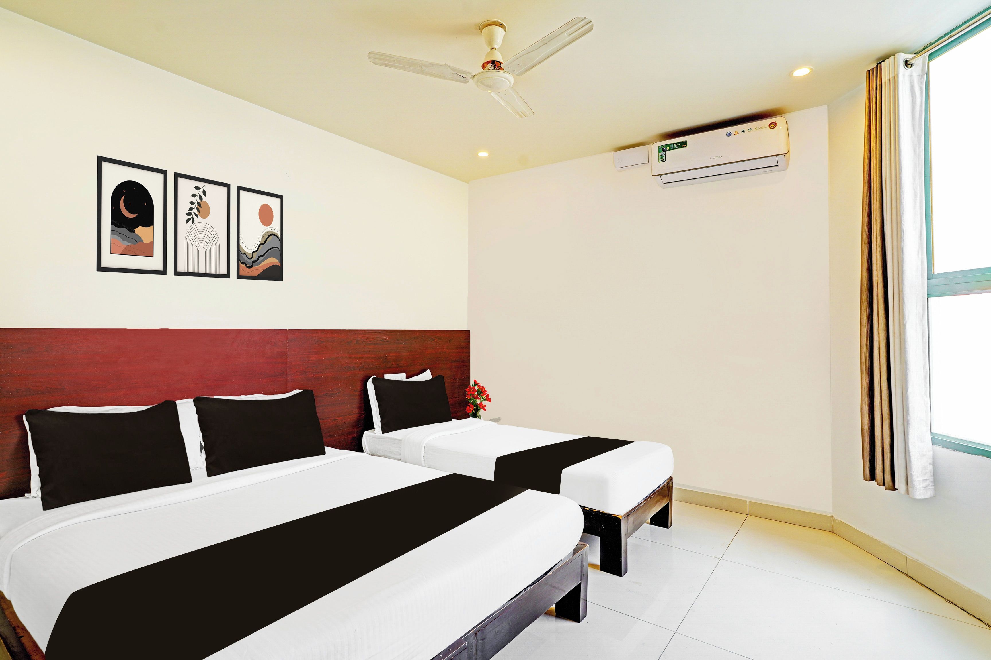 Habitación de hotel con dos camas, ventilador de techo, unidad de aire acondicionado y cuadros en la pared.