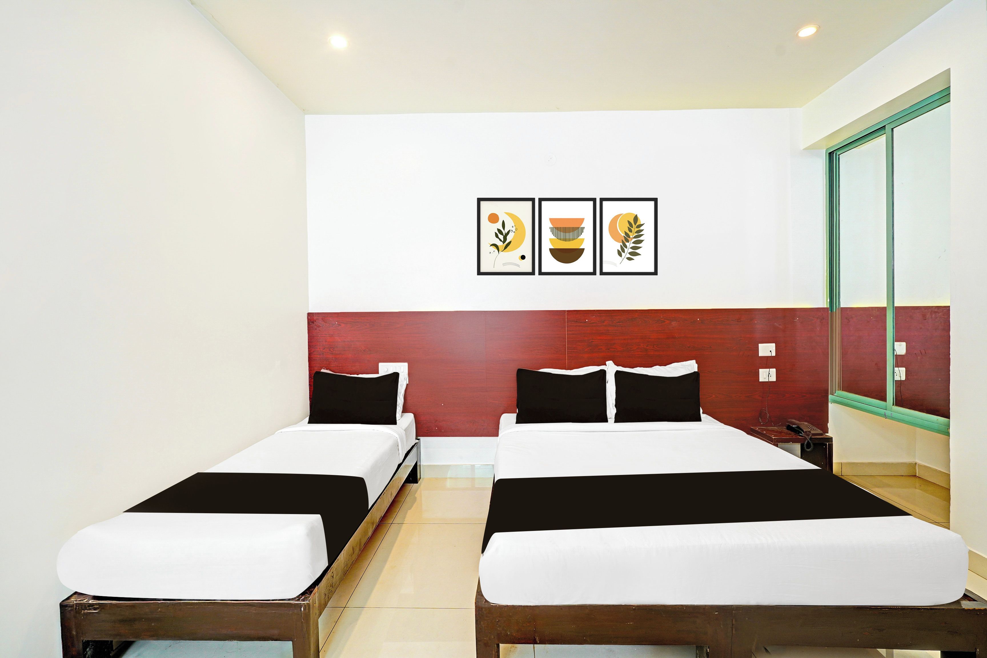 Habitación de hotel con dos camas, una pared de acento roja y tres cuadros enmarcados sobre las camas.