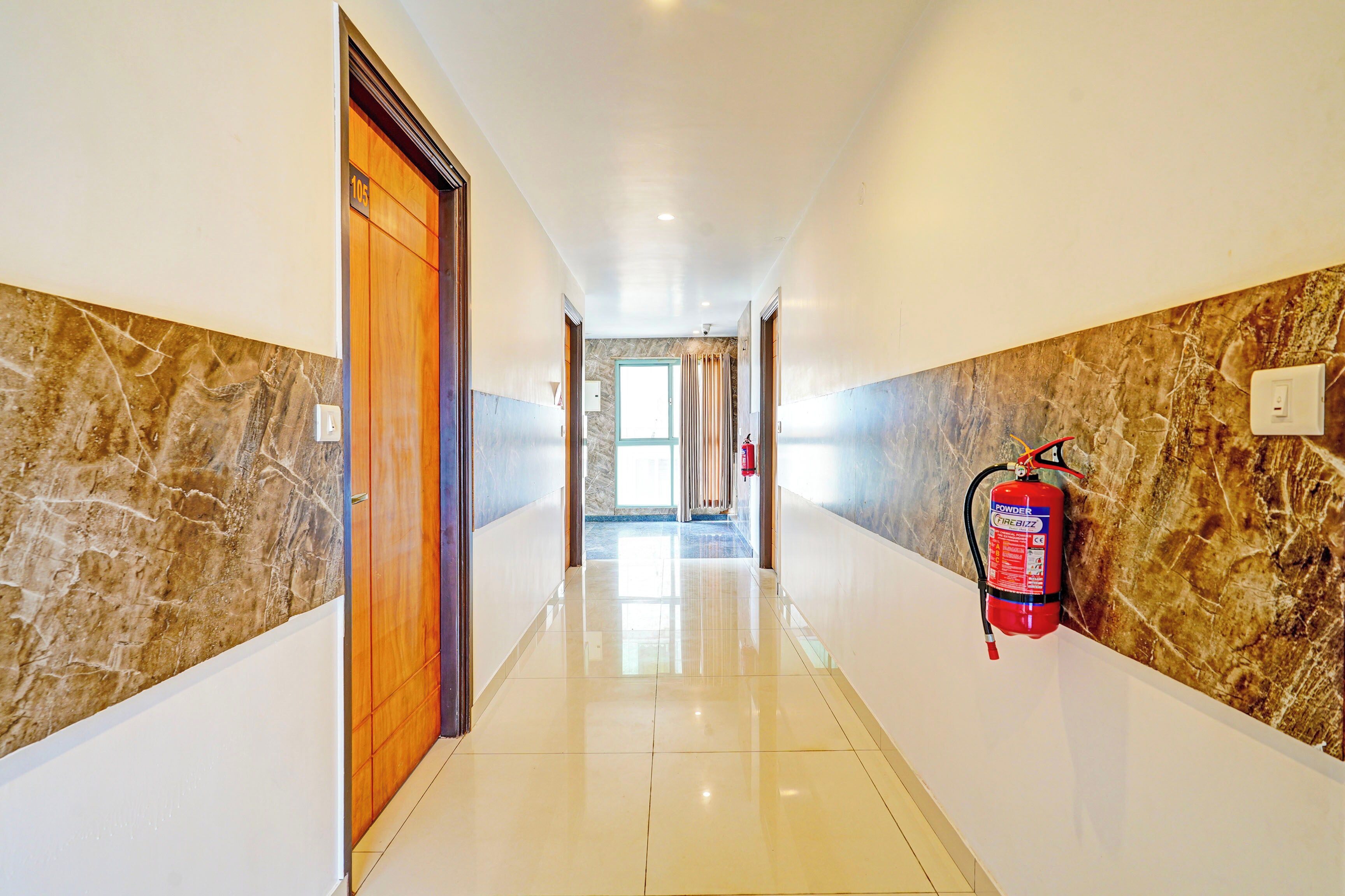 A hotel hallway with a fire extinguisher mounted on the wall, a door on the left, and a tiled floor.