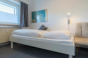 Ein Zimmer mit einem Einzelbett, einem Fenster, einer Karte an der Wand und einem Stuhl.
