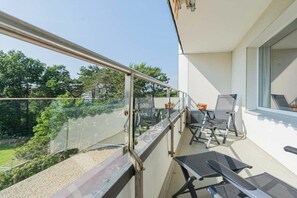 Ein Balkon mit Glasgeländer, Gartenmöbeln und Blick auf Grünflächen.